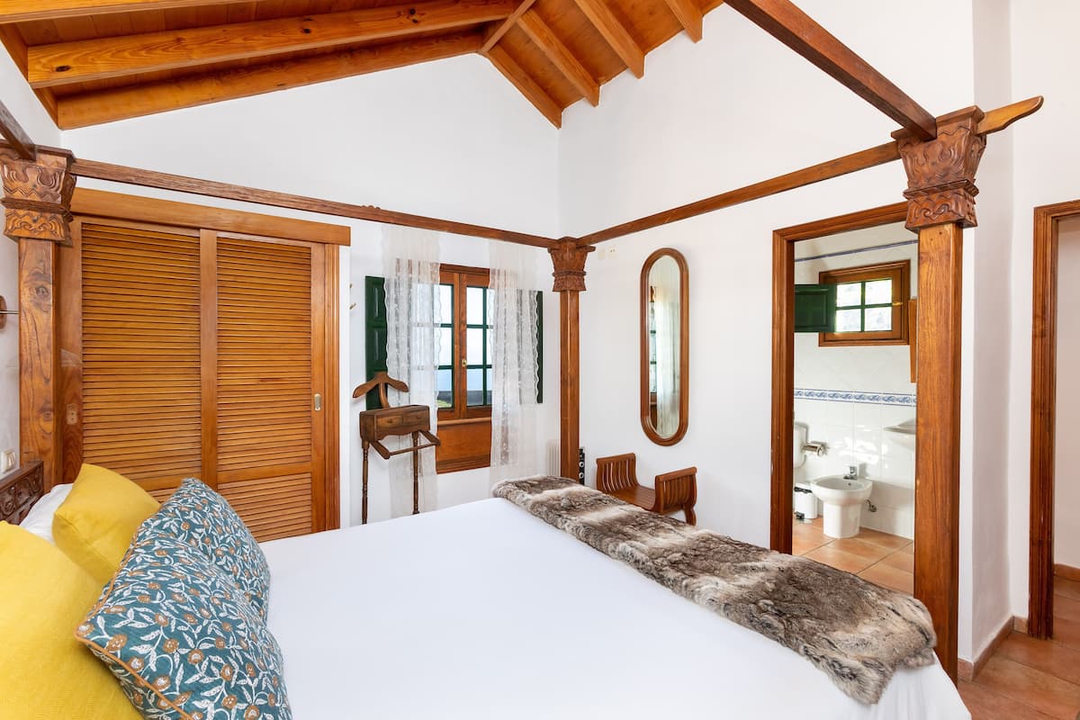 A bedroom with a large bed, wooden wardrobe, and a mirror.