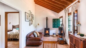 A cozy living room with a fireplace, a sofa, a wooden cabinet, and a bed in the adjacent room. - Las Casas del Chorro (Agulo)