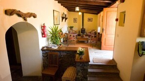 Un intérieur chaleureux avec un banc en pierre, un foyer et un escalier en bois menant à un espace repas équipé de chaises et d’une table.