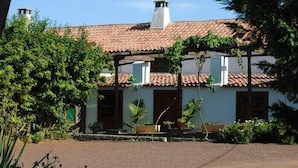 Il s’agit d’un bâtiment traditionnel, doté d’un toit en tuiles, d’une entrée centrale et d’un petit porche agrémenté de plantes en pot.
