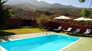 Une piscine dotée de chaises longues et de parasols, entourée d’un jardin aménagé et offrant une vue sur les montagnes.