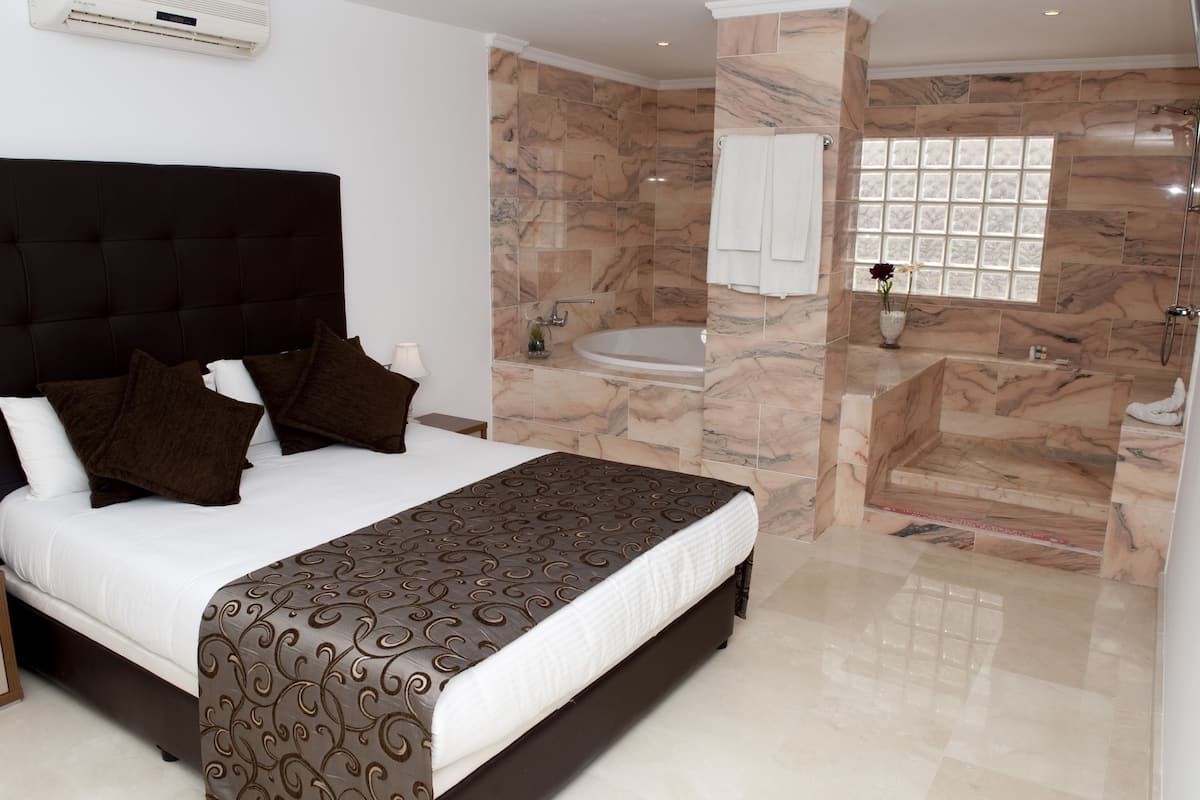 A bedroom with a large bed, a bathroom with a bathtub and a shower, and marble walls.