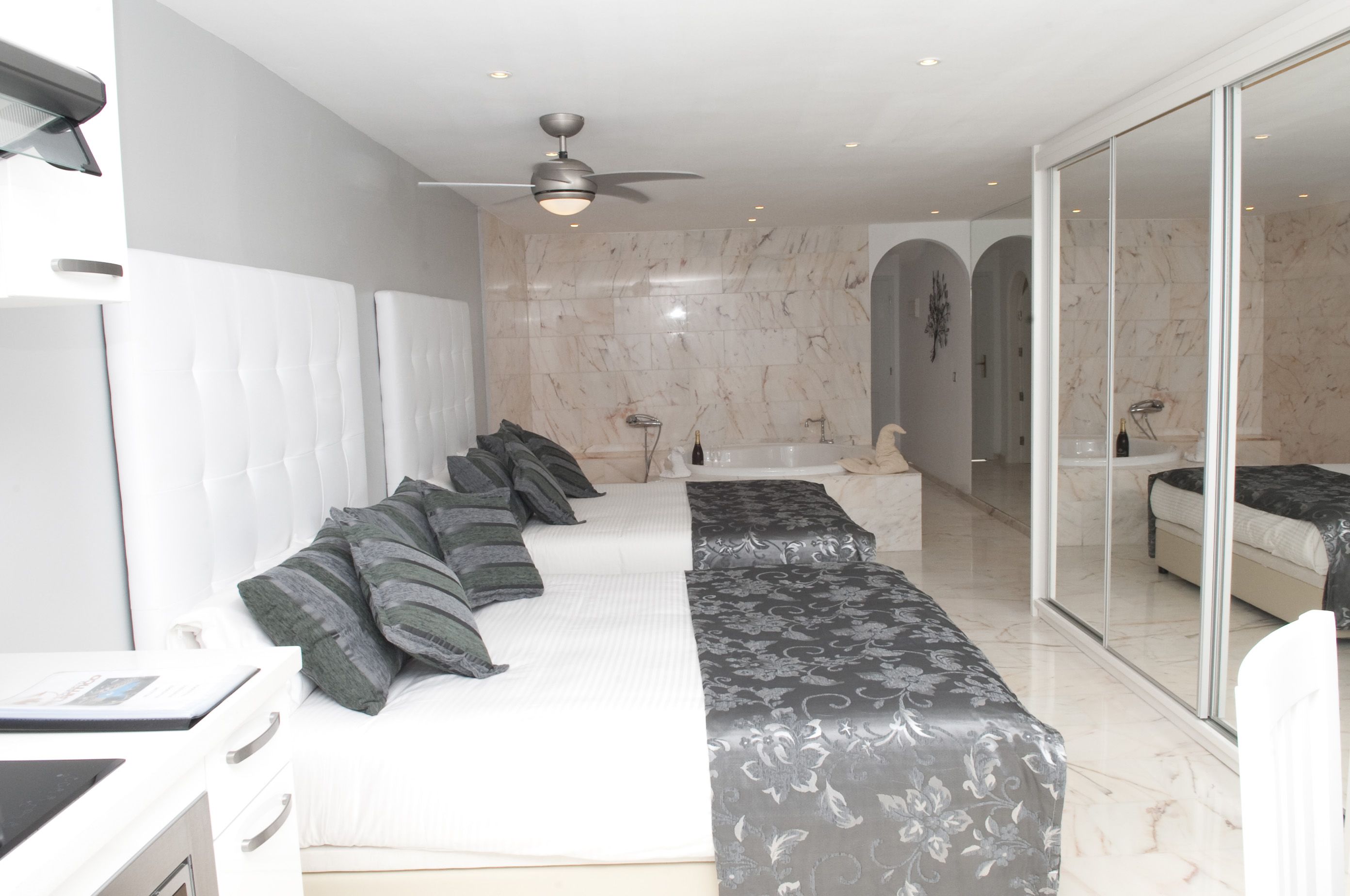A modern bedroom with a large bed, a separate sofa bed, a walk-in closet, and a bathroom with a bathtub.