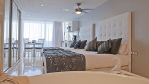 A modern hotel room with a large bed, a separate sofa, a dining area with a table and chairs, and a bathroom with a bathtub. - Club Puerto Atlantico (Mogan)
