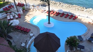 A pool area with red lounge chairs, a palm tree, and a white fence. - Club Puerto Atlantico (Mogan)