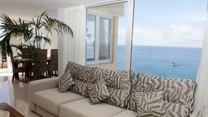 A living room with a sofa, a dining table, chairs, and a large window overlooking the sea. - Club Puerto Atlantico (Mogan)