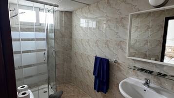 A bathroom with a glass shower enclosure, a toilet, a sink, and a marble-tiled wall.