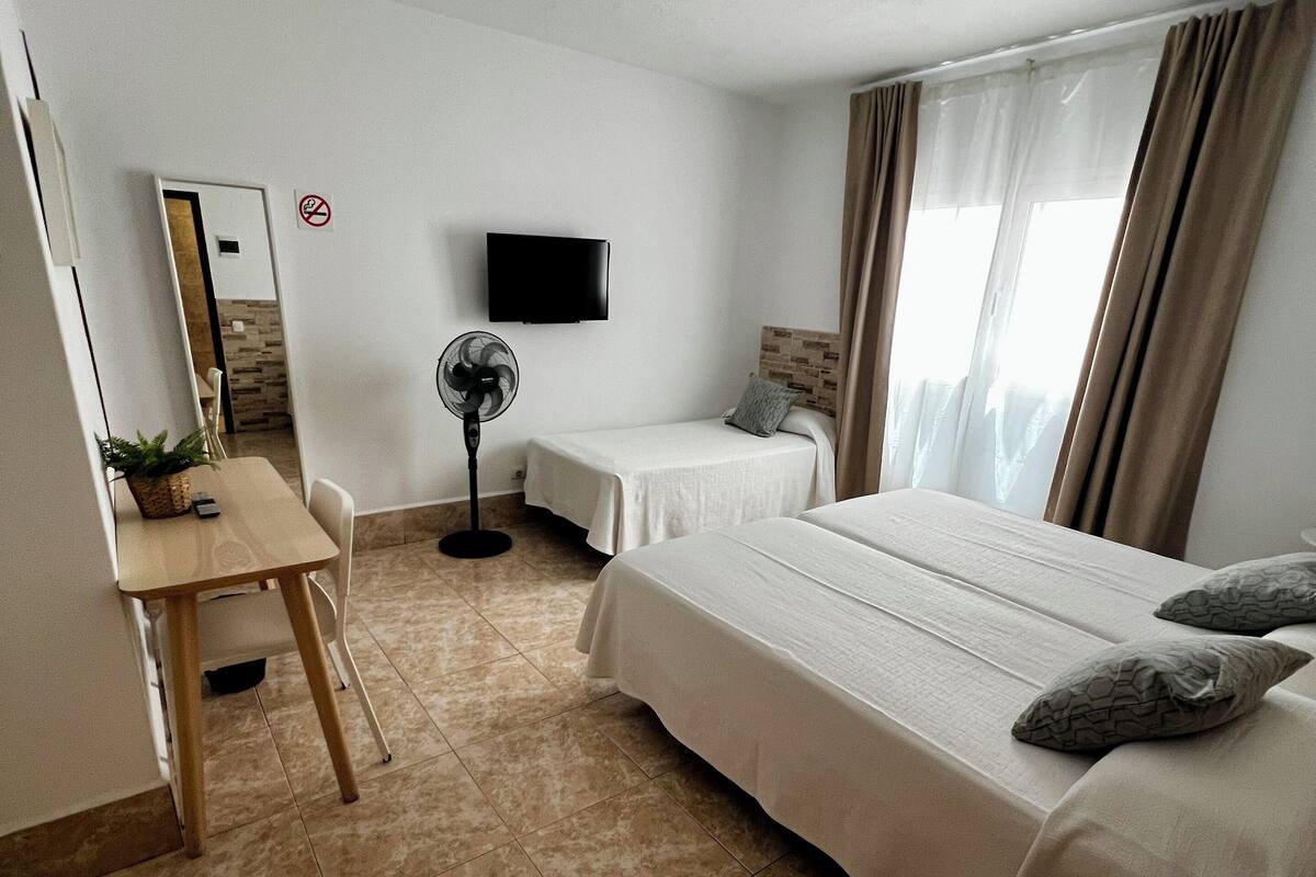 Habitación de hotel con cama, escritorio, silla, televisor y ventilador.