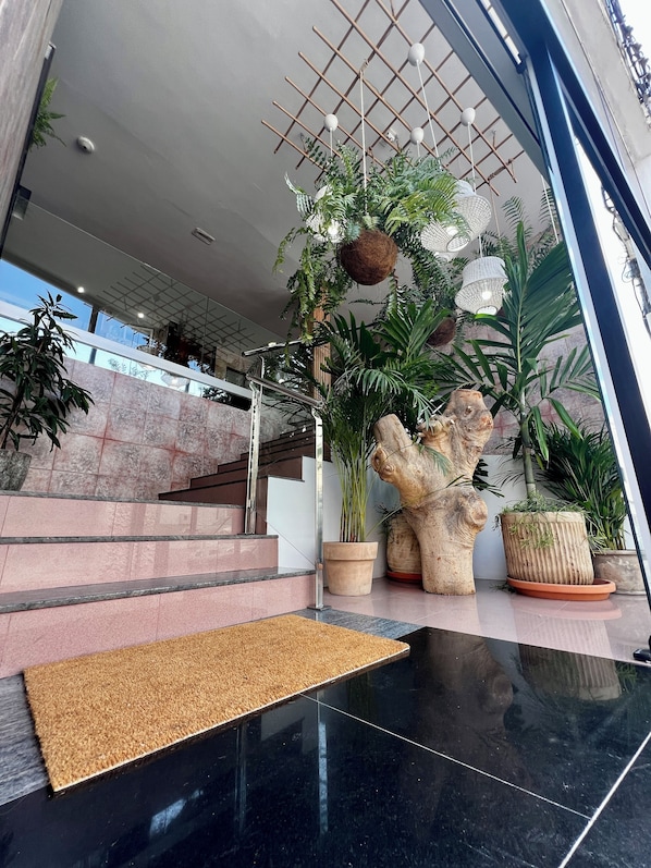 Una entrada de hotel moderna con una escalera de mármol, plantas en macetas y una gran escultura decorativa.