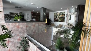 A modern lobby with a marble reception desk, potted plants, and a staircase leading to upper floors. - Hostal Residencia Cardona (Arrecife)