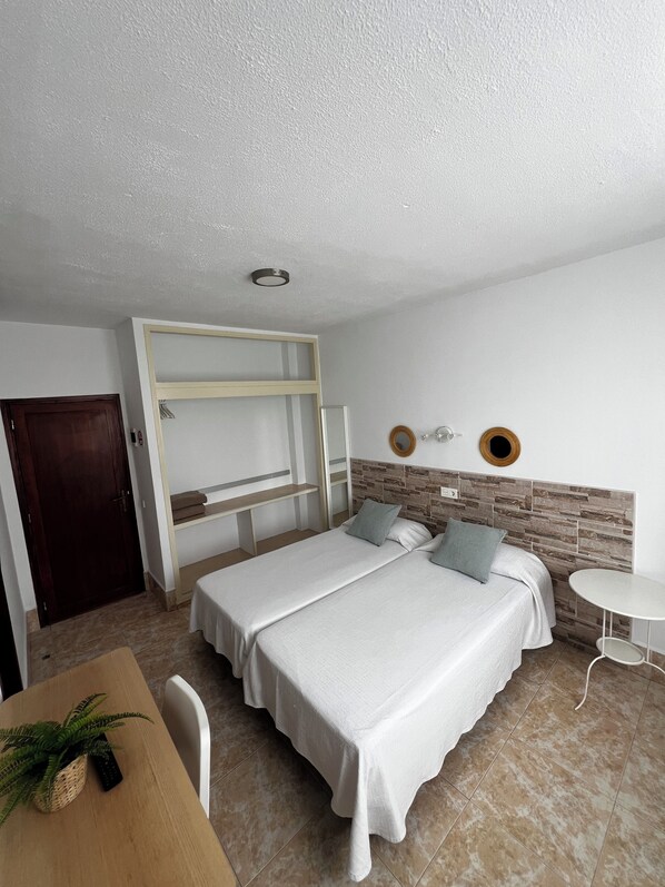 A bedroom with a bed, a desk, and a chair. There is a door and a wall-mounted shelf.