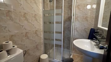 Un baño con inodoro, lavamanos, cabina de ducha y paredes de mármol.