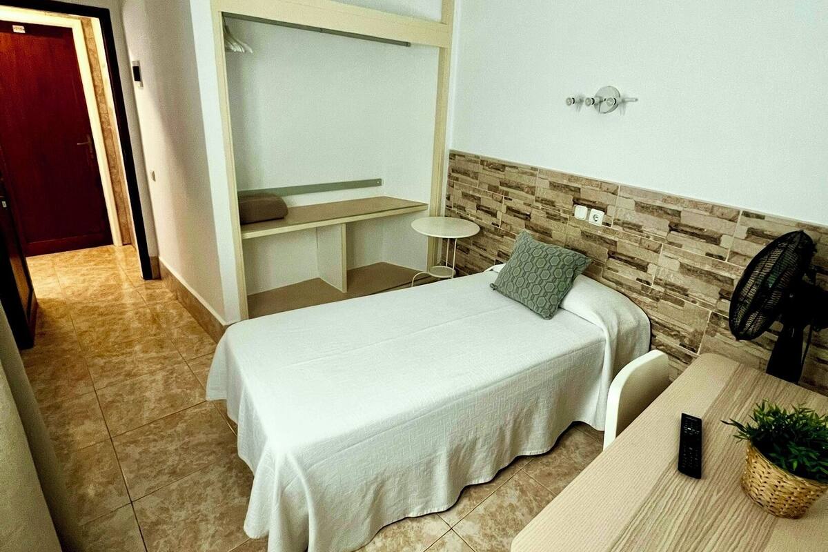 Un dormitorio pequeño y ordenado con cama, mesita de noche y estante en la pared.