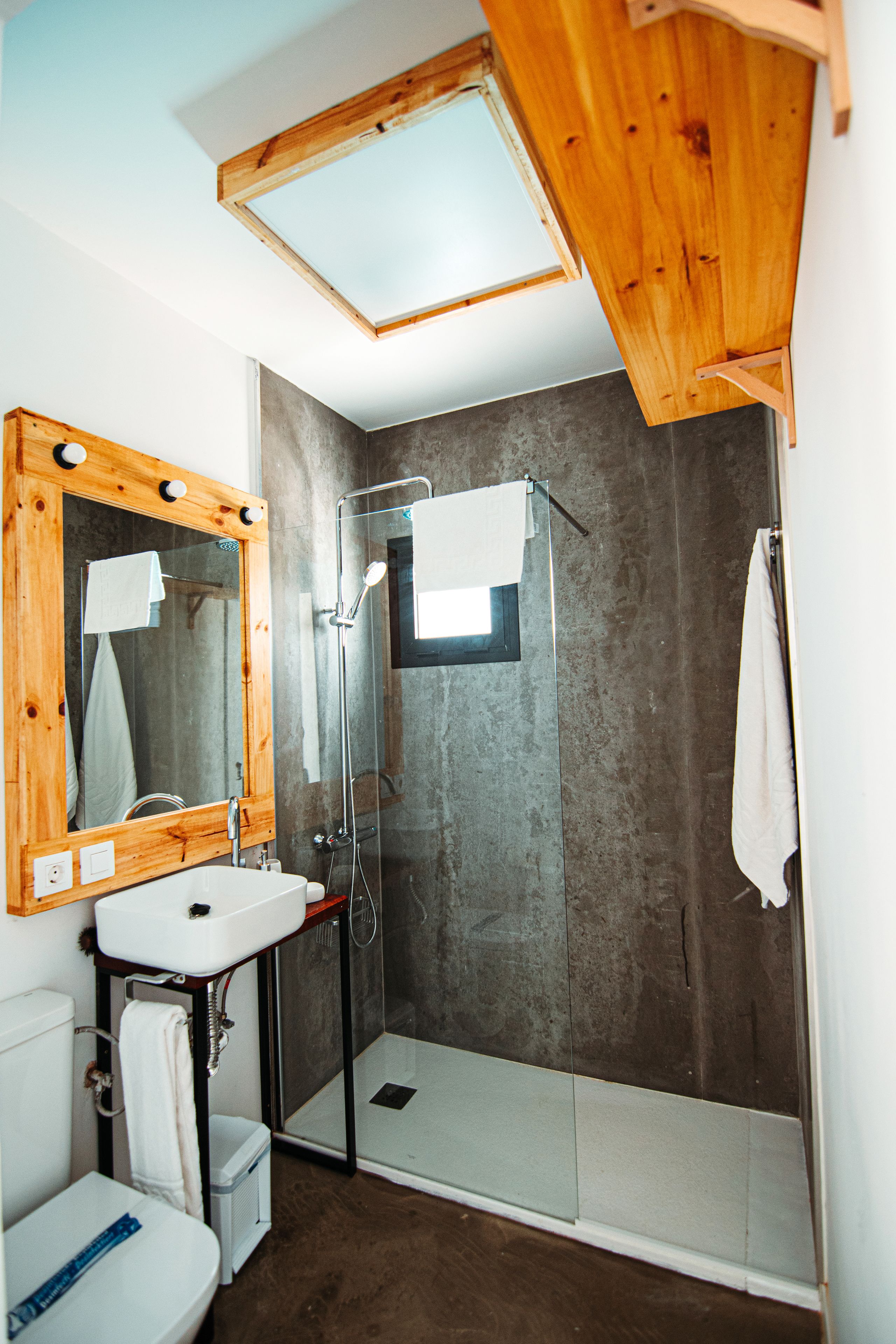 Une salle de bain avec un miroir encadré en bois, un lavabo blanc, une douche et une serviette accrochée au mur.