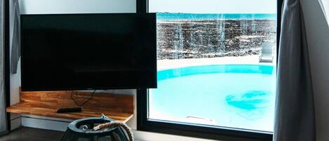 Une chambre dotée d’une grande fenêtre donnant sur une piscine et offrant une vue sur la plage.