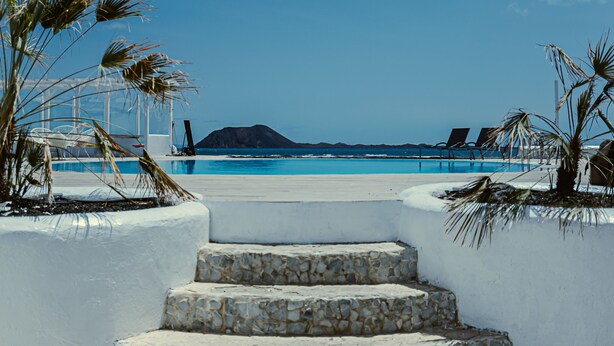 Una escalera de piedra que baja a una playa con sillas de descanso y palmeras.
