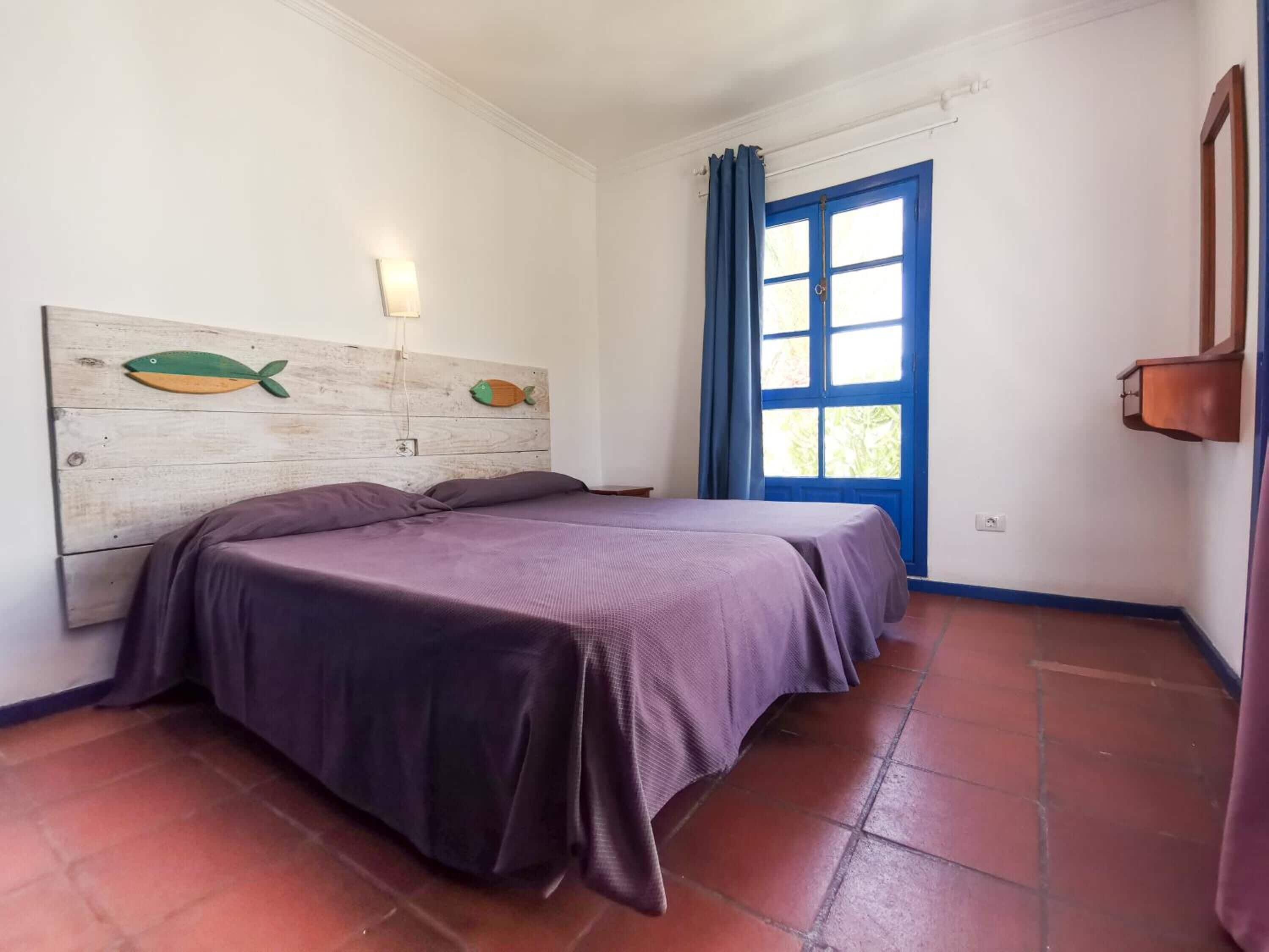Ein Zimmer mit einem Bett, einer Wandleuchte, einer blauen Tür und einem hölzernen Kopfteil mit Fischornamenten.
