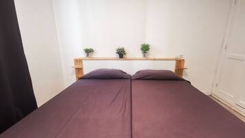 A bed with a wooden headboard, two potted plants on a shelf above, and a white door to the right.
