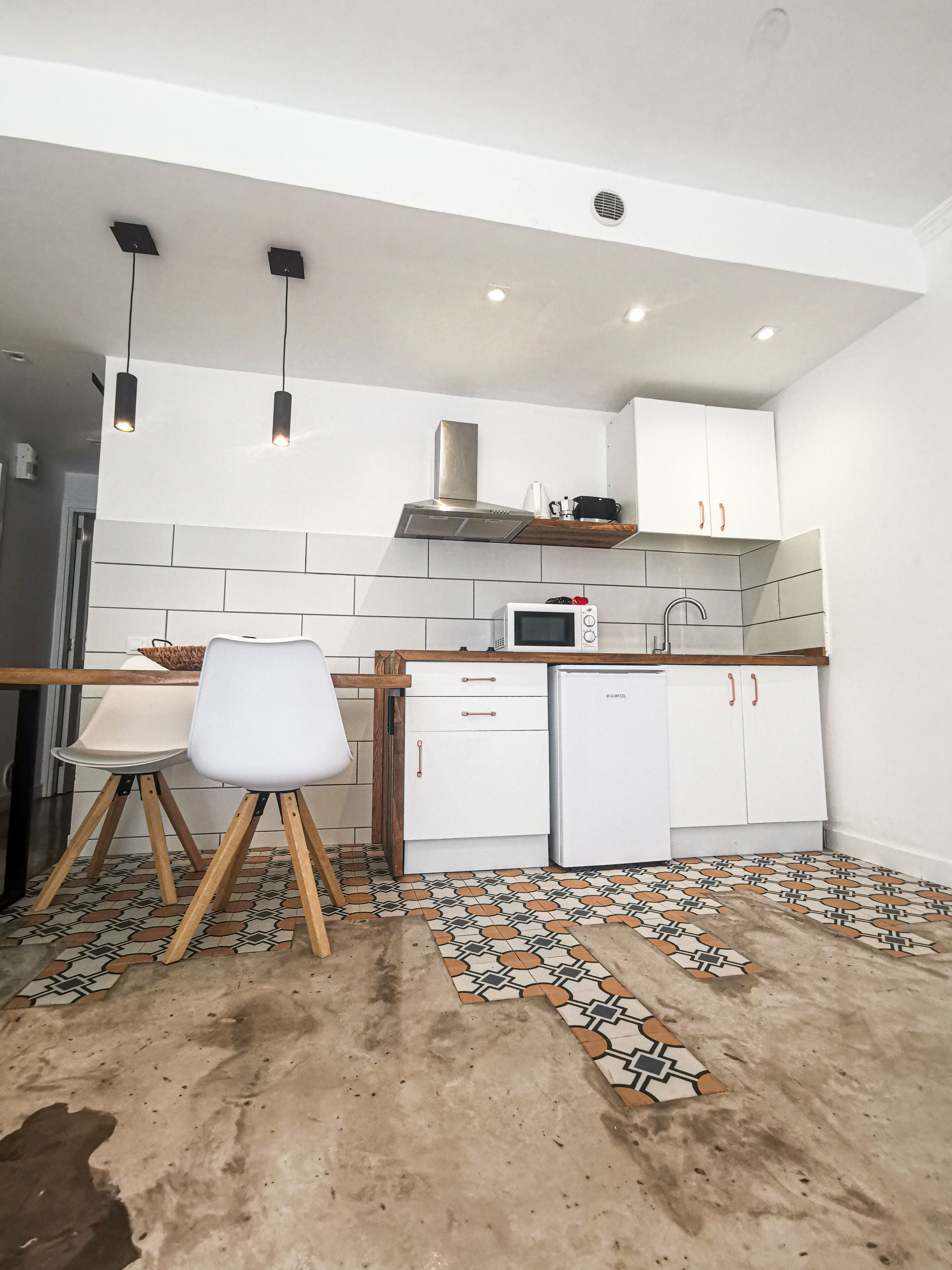 Une cuisine moderne avec des meubles blancs, un four à micro-ondes et un évier. On y trouve une table à manger en bois, accompagnée de chaises.