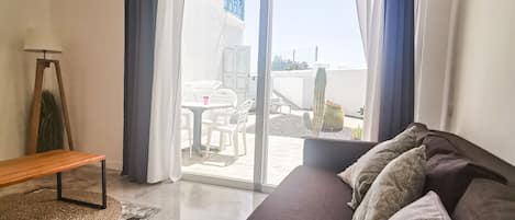 A modern bedroom with a large bed, a bench, and a view of the outside balcony.