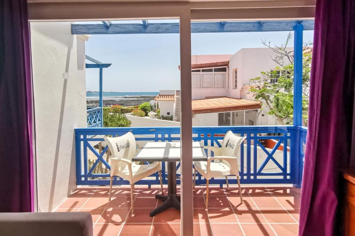 A balcony with a table and chairs, a view of the sea, and a building in the background.