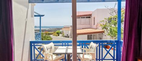 A balcony with a table and chairs, a view of the sea, and a building in the background.