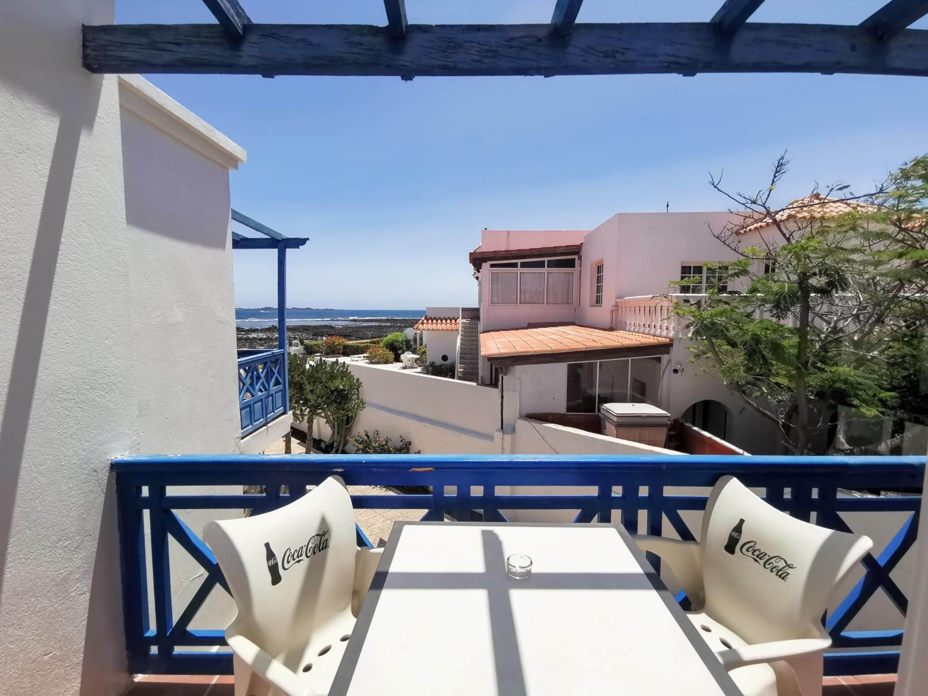 A balcony with a table and chairs, overlooking a coastal area with buildings and a view of the sea.