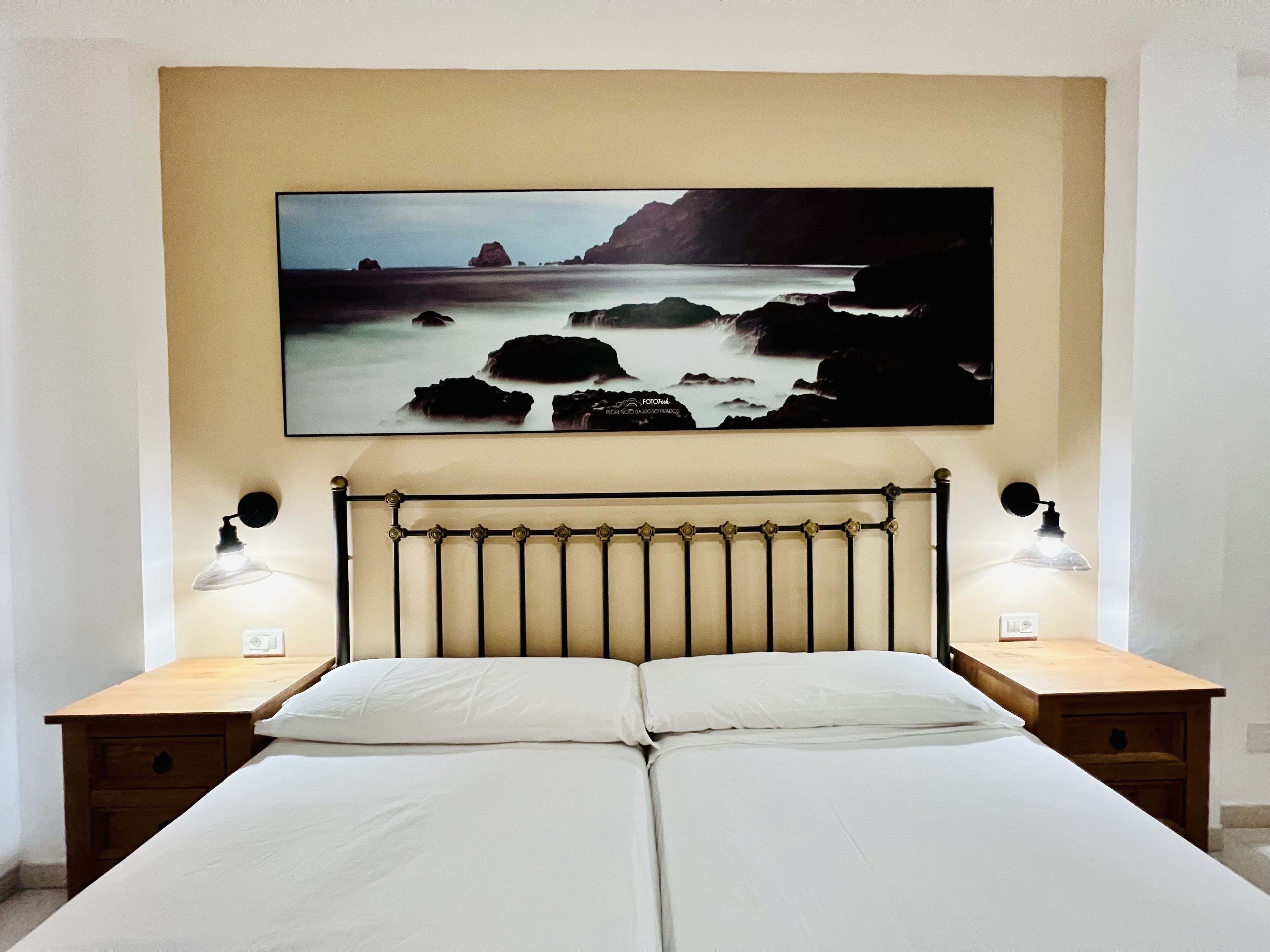 Un dormitorio con una cama, dos mesitas de noche y un cuadro colgado en la pared que muestra una escena costera.
