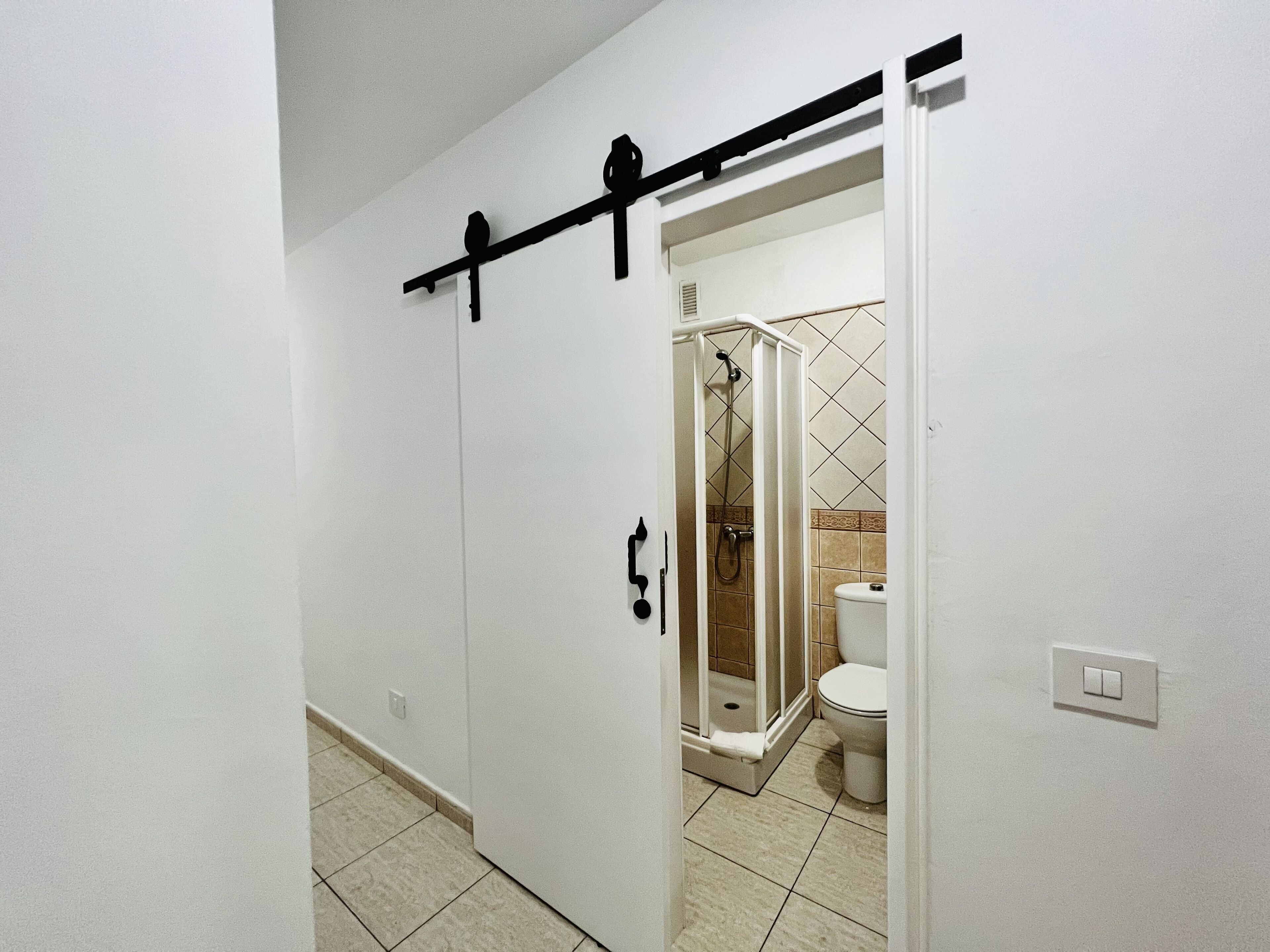 Une salle de bain avec une douche, des toilettes et une porte blanche dotée d’une poignée noire.