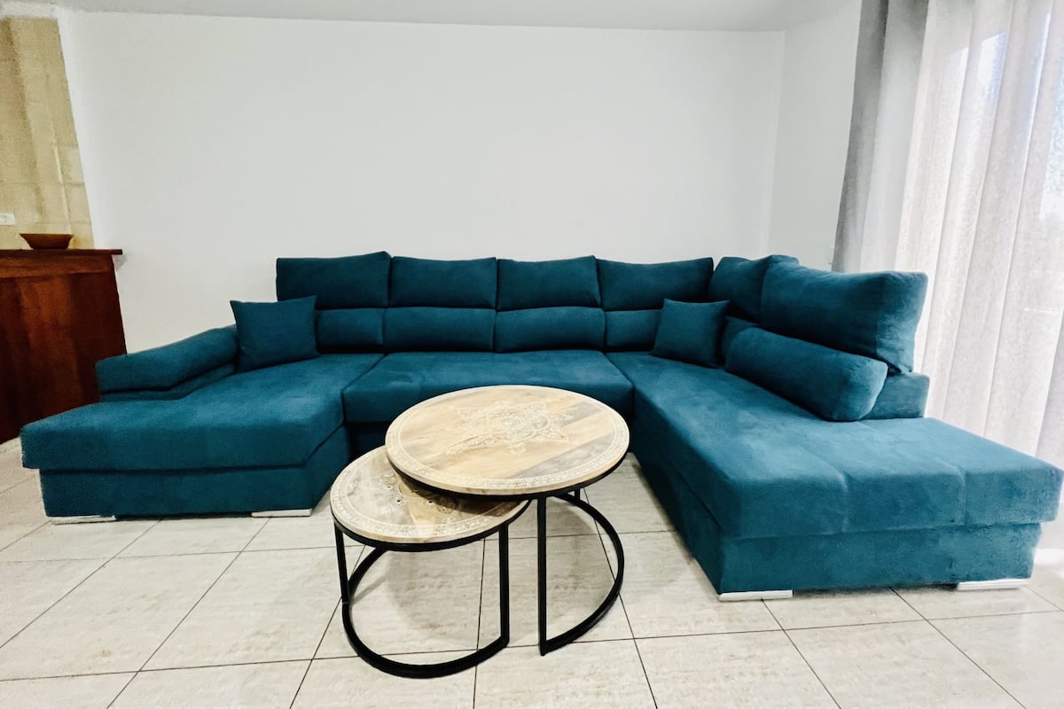 A blue sectional sofa with a round coffee table in a room with tiled flooring.
