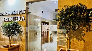 De ingang van een hotel met een receptiebalie, een bord met 'Apartamentos Frontera' en twee potplanten.