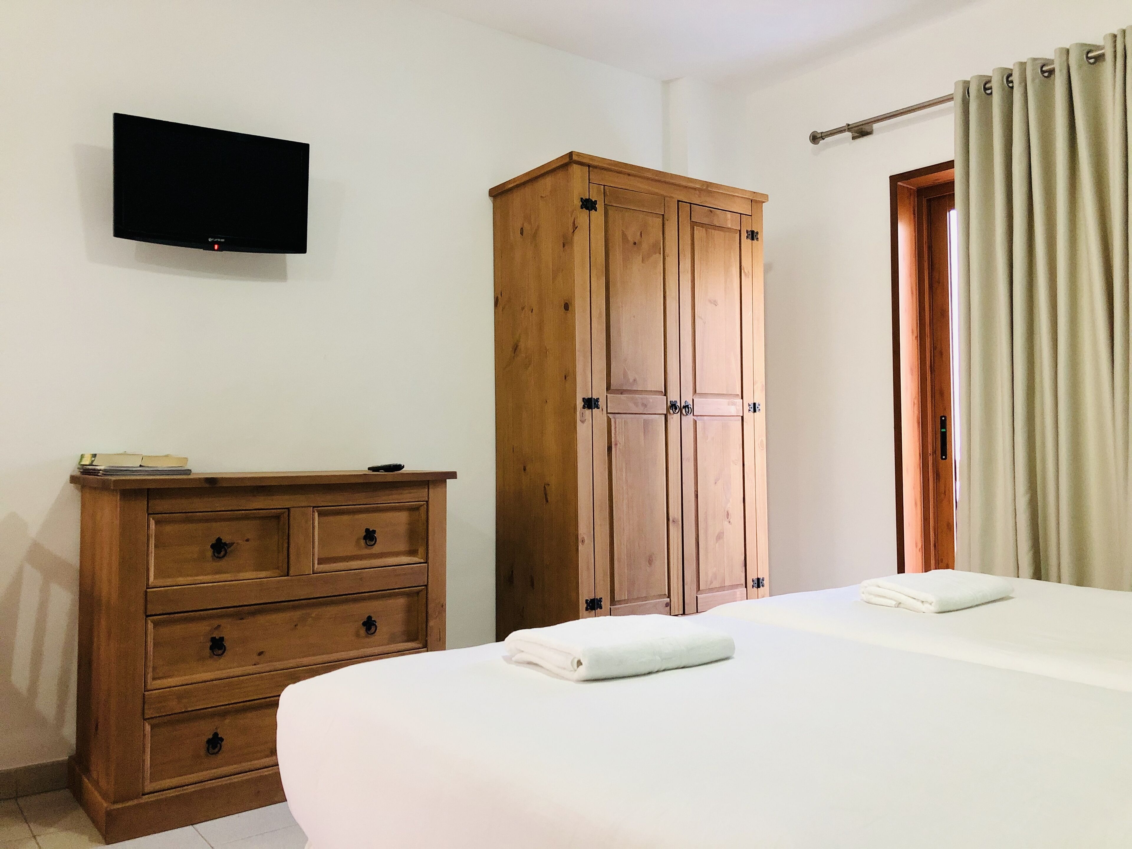 A bedroom with a wooden wardrobe, a flat-screen TV, and a bed with a white duvet.