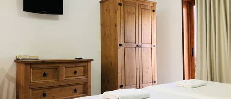 A bedroom with a wooden wardrobe, a flat-screen TV, and a bed with a white duvet.