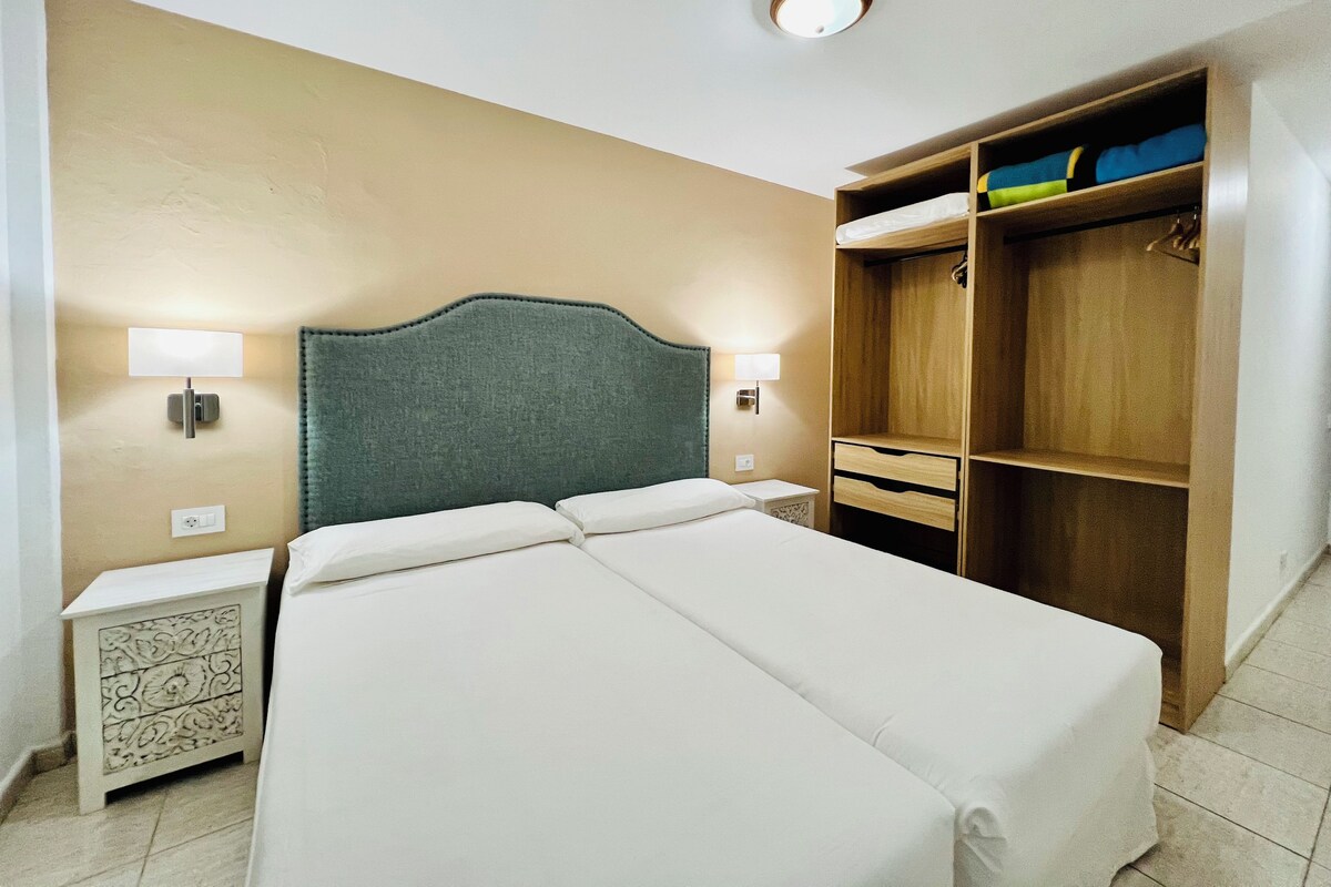 Habitación de hotel con cama doble, lámparas de noche, armario de madera y mesita de noche con un diseño decorativo.