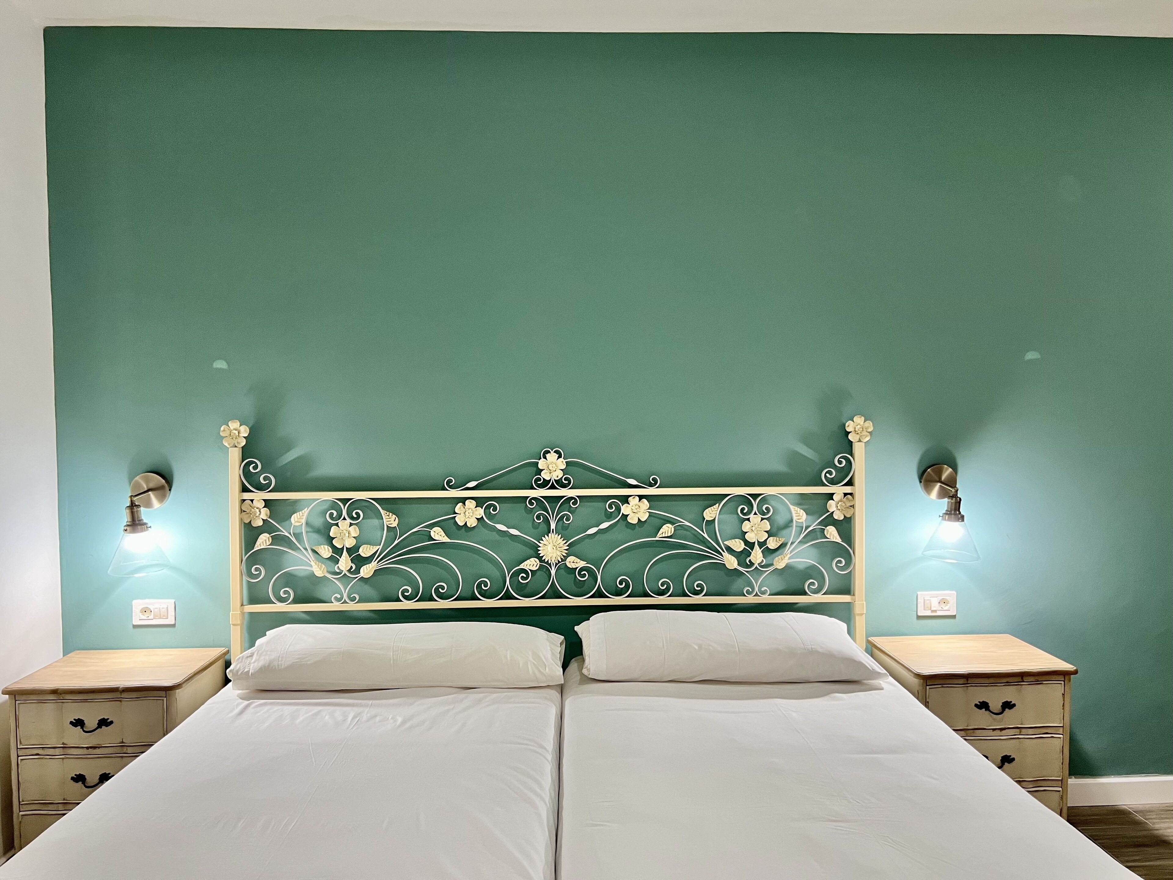 Un lit double avec une tête de lit décorative, deux tables de chevet et des lampes fixées au mur.