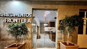 De ingang van een hotel genaamd "Apartamentos Frontera", met een receptiebalie van binnenuit zichtbaar.