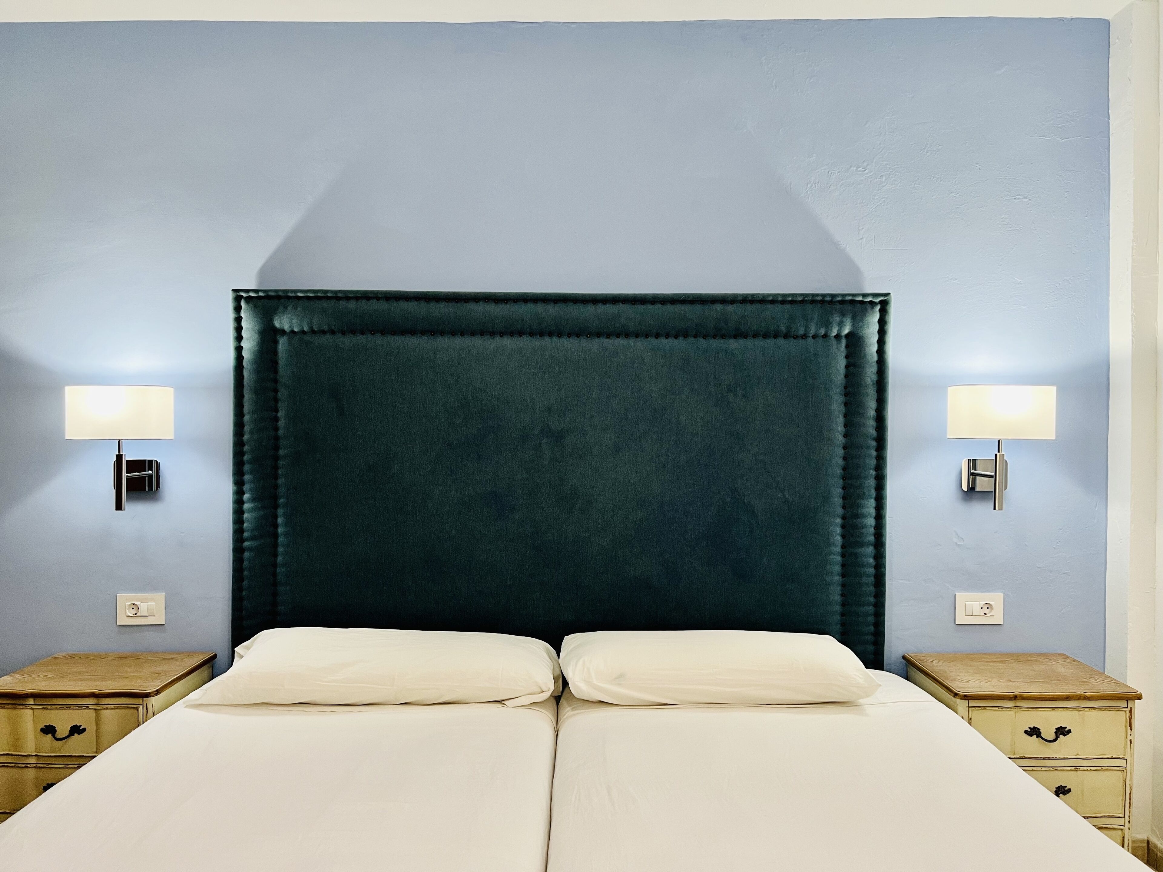 A double bed with a dark headboard, two bedside tables with lamps, and a light blue wall.