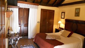 A bedroom with a bed, a nightstand, a lamp, a wooden headboard, a door, and a small table with a lamp and a bottle. - Casa Rural Anton Piche (Granadilla de Abona)