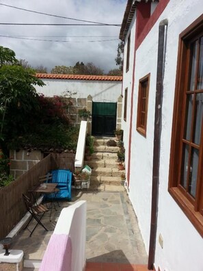 A narrow courtyard with a stone staircase leading to a green door, a wooden fence, and a blue barrel. - Casa Rural Anton Piche (Granadilla de Abona)
