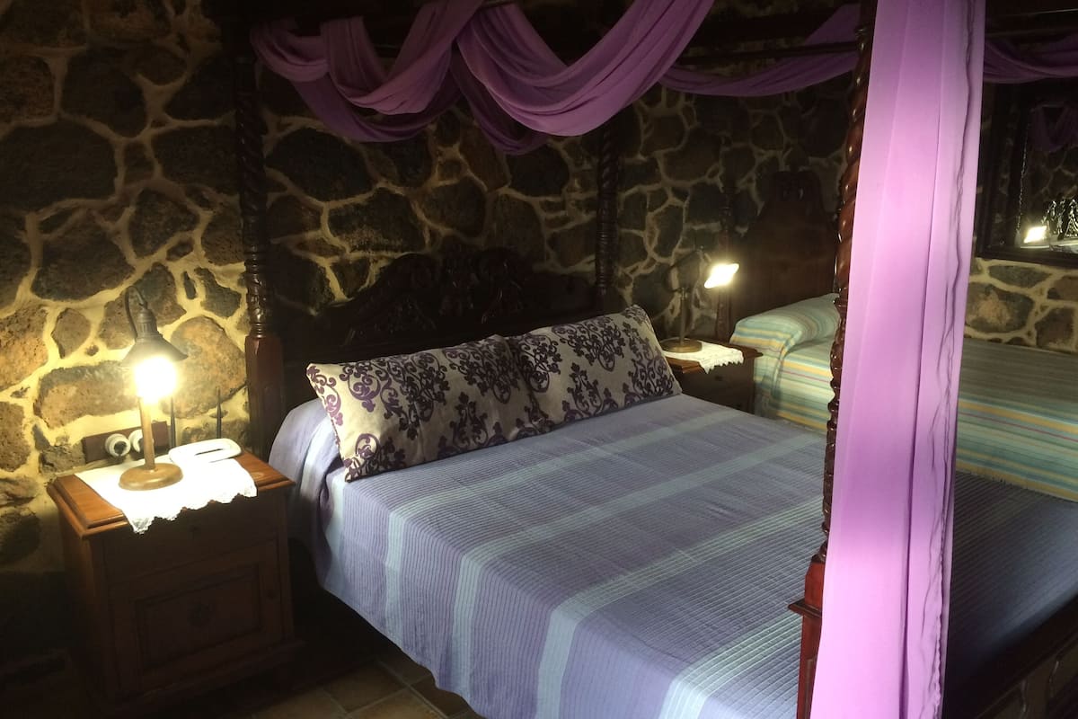 A stone-walled bedroom with a bed, nightstands, and a canopy.