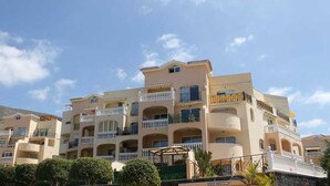 Un hotel de varios pisos con balcones, un espacio al aire libre cubierto y un paisaje montañoso de fondo.