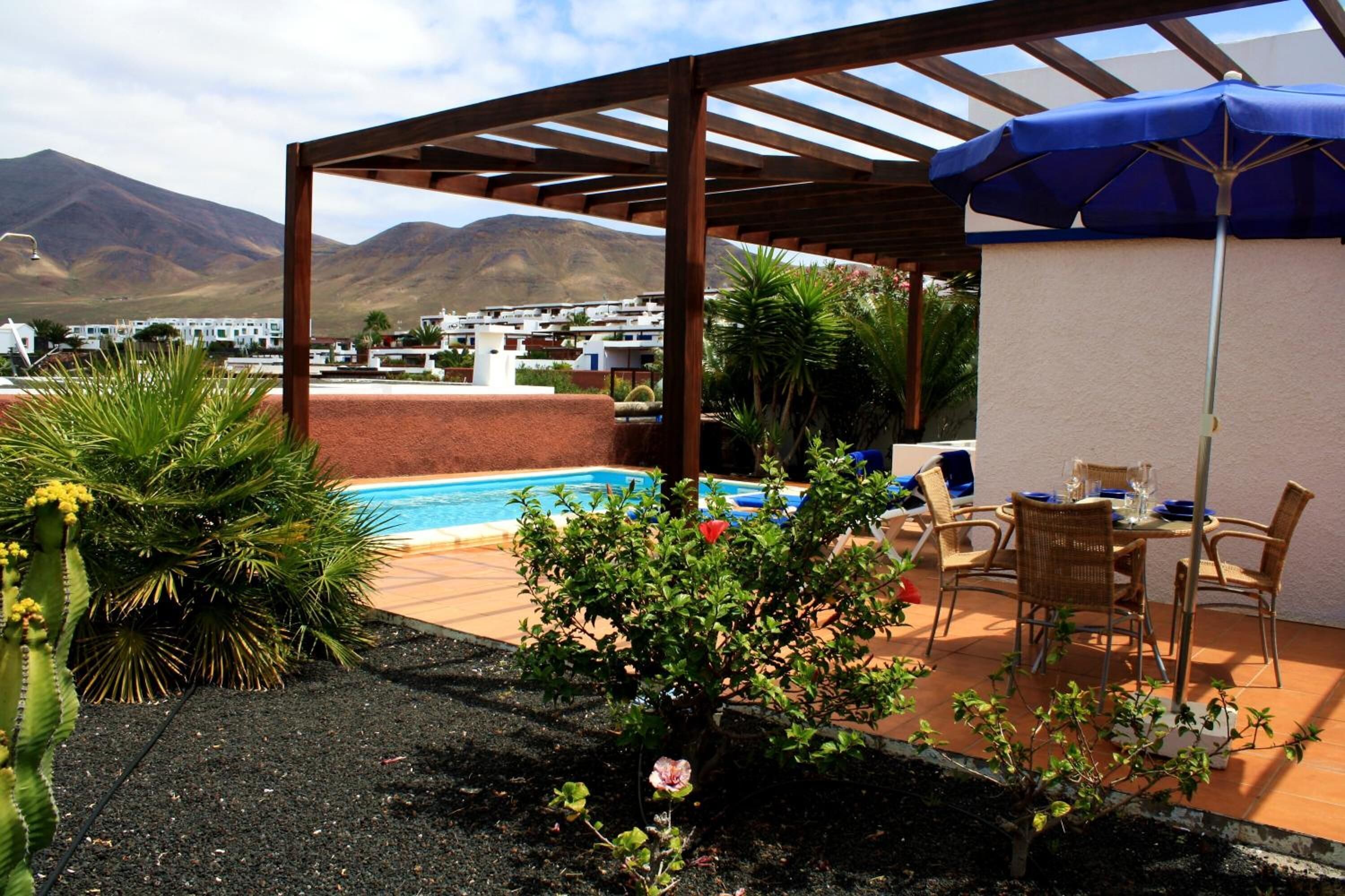 Un espacio de estar al aire libre cubierto con piscina, rodeado de plantas y vistas a la montaña.