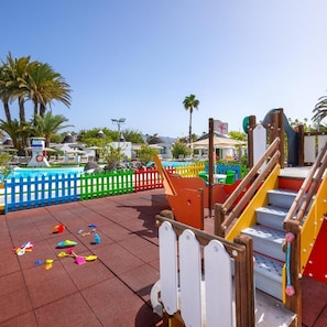 A playground with colorful play structures and a pool in the background.