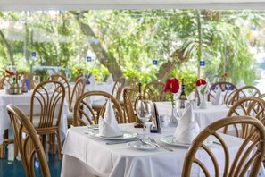 A restaurant setting with tables set for dining, featuring white tablecloths and wicker chairs. - The Mur Bungalows Parque Romántico (San Bartolome de Tirajana)