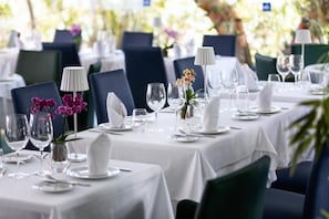A restaurant with tables set for dining, featuring white tablecloths, chairs, and glassware.