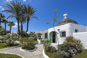A white building with a dome roof, surrounded by palm trees and flowering plants. - The Mur Bungalows Parque Romántico (San Bartolome de Tirajana)