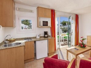 Eine kompakte Küche mit Spüle, Mikrowelle und kleinem Kühlschrank. Ein Essbereich mit Tisch und Stühlen lädt zum Verweilen ein, und ein Glastür bietet Blick ins Freie.