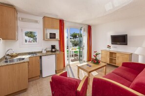 A compact living space with a kitchenette, a dining area, and a seating area with a red sofa. - The Mur Bungalows Parque Romántico (San Bartolome de Tirajana)
