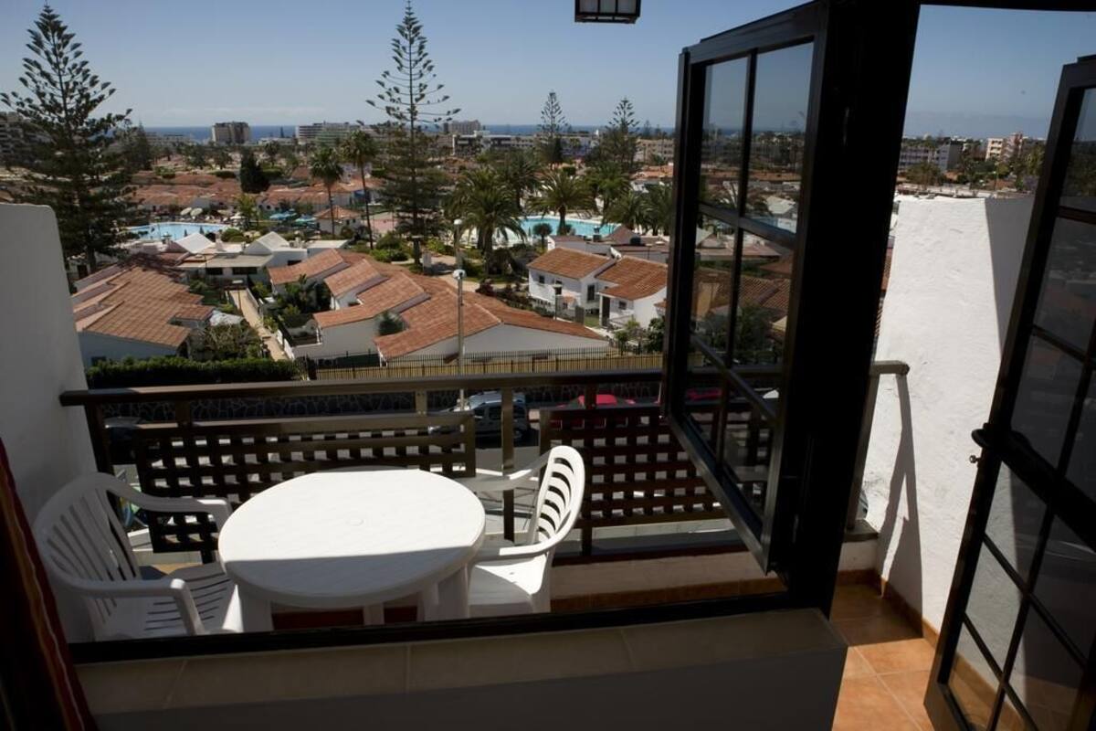 Ein Balkon mit Tisch und Stühlen, der auf einen Wohnbereich mit Häusern und blauem Himmel blickt.