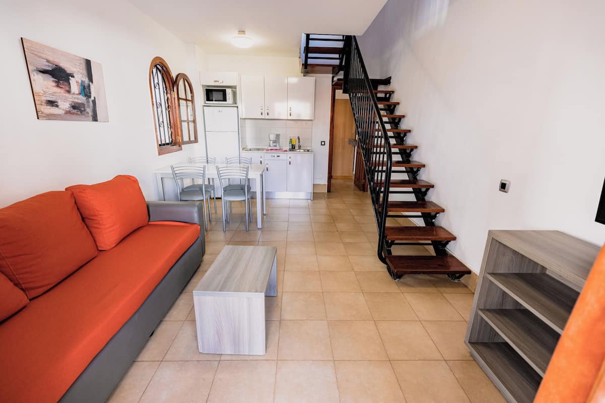 Una sala de estar moderna con un sofá, una mesa de centro y una escalera que lleva a una zona de cocina.